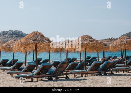 Kalafati, Griechenland - 23. September 2019: Blaue Sonnenliegen unter Sonnenschirmen am Strand von Kalafati, einem beliebten Strand auf Mykonos, der für Wassersport bekannt ist, an einem sonnigen Ort Stockfoto