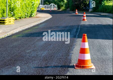 Baukegel markieren einen Teil der Straße mit einer Schicht aus frischem Asphalt. Stockfoto