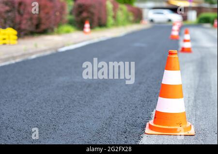 Baukegel markieren einen Teil der Straße mit einer Schicht aus frischem Asphalt. Stockfoto