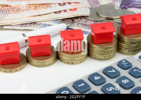 Rote Häuser, die auf einer Münze sitzen, mit einem Stift und einem Rechner, um die Hausfinanzierung im Vereinigten Königreich zu symbolisieren. Stockfoto