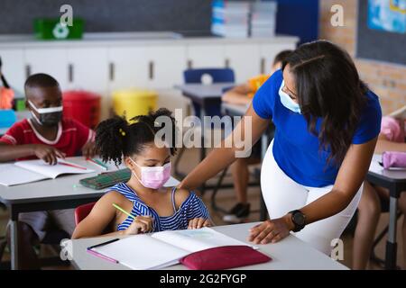 afroamerikanische Lehrerin mit Gesichtsmaske, die afroamerikanisches Mädchen in der Schule unterrichtet Stockfoto