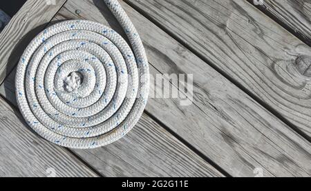 Nahaufnahme eines weißen Seils, das auf einem verwitterten Holzdock aufwickelt ist. Speicherplatz kopieren. Stockfoto