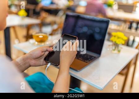 Junge Frau, die Mobiltelefon benutzt, während sie den Akku lädt Stockfoto