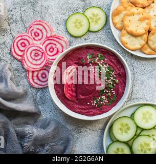 Schüssel Rübenhummus, Gemüse und Cracker auf grauem Hintergrund. Stockfoto