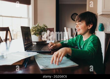 Glücklicher Junge, der auf der Schularbeit online am Computer am Küchentisch arbeitet. Stockfoto