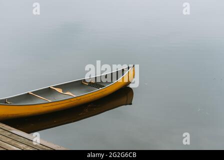 Leeres gelbes Kanu an einem hölzernen Dock an einem ruhigen See in Kanada. Stockfoto