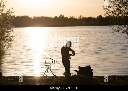 Eine Fischersilhouette beim Fischen bei Sonnenuntergang. Stockfoto