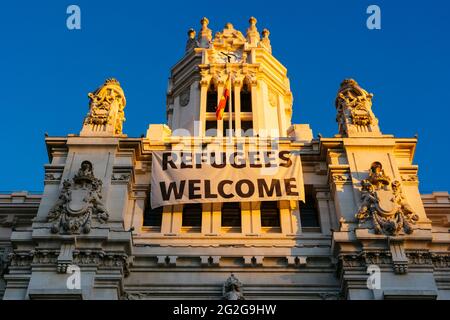 Zentraler Turm mit dem Banner 'Flüchtlinge willkommen'. Cibeles Palace - Palacio de Cibeles ist ein Komplex aus zwei Gebäuden mit weißen Fassaden und ist loc Stockfoto