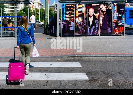 Frau geht mit einem fahrbaren Koffer ein Zebrastreifen auf der Plaza de Cibeles. Madrid, Comunidad de madrid, Spanien, Europa Stockfoto