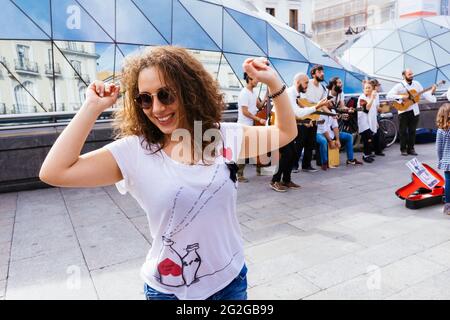 Junge Frau tanzt vor einer Aufführung von Straßenmusikern in Puerta del Sol. Die Puerta del Sol, das Tor der Sonne, ist ein öffentlicher Platz in Madrid, Stockfoto