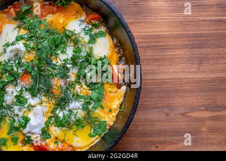 Pochierte Eier mit Tomaten und Gewürzen, genannt 'Shakshuka', gekocht in einer gusseisernen Pfanne, auf einem Holztisch. Rustikaler Stil. Draufsicht. Stockfoto