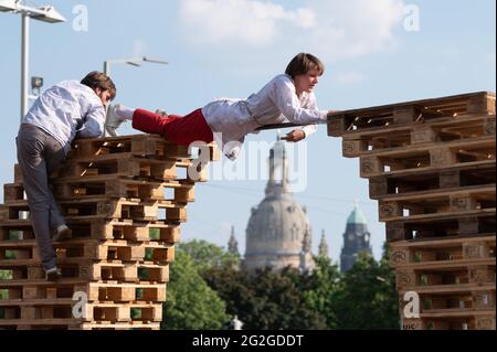 Dresden, Deutschland. Juni 2021. Künstler der kleinen Zirkusgruppe 'FahrAway' aus der Schweiz klettern bei einer Performance vor der Kulisse der Frauenkirche auf einen Stapel Europaletten. Die Performance ist Teil des Programms des Societatheaters Dresden. Quelle: Sebastian Kahnert/dpa-Zentralbild/dpa/Alamy Live News Stockfoto