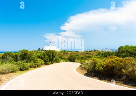 Atemberaubende Aussicht ein weißer Leuchtturm, umgeben von einer grünen Vegetation, an einem schönen sonnigen Tag mit einer Straße im Vordergrund. Cala Del Faro, Sardinien. Stockfoto