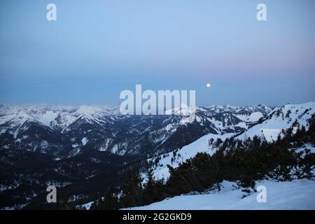 Von der Auerspitze Richtung Karwendelgebirge südwestlich, der unterste Mond über den Bergen von links nach rechts Österr. Schinder 1807m, in der Mitte des Risserkogels (1825m), Blankenstein (1768m), Bendiktenwand (1799m), Setzberg, Hirschberg, Wallberg, davor die Rotwand mit dem Rotwandhaus kurz vor Sonnenaufgang. Europa, Deutschland, Bayern, Oberbayern, Bayrische Alpen, Mangfall Mountains, Spitzingsee Stockfoto