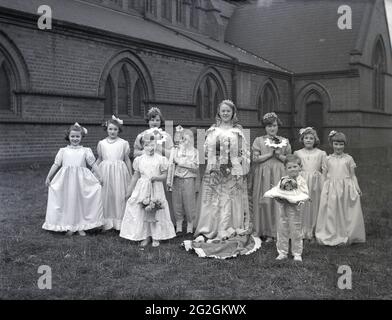 1956, historischer Karneval der May Queen, draußen auf dem Gelände einer Kirche, steht eine Gruppe von Kindern für ein Foto in den hübschen Kleidern, Kleidern und Outfits, die sie bei der May Day Parade der Stadt, Leeds, England, Großbritannien, tragen werden. Stockfoto