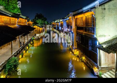 Nachtansicht der beleuchteten traditionellen chinesischen Häuser, des Kanals und der Steinbrücke in der historischen malerischen Wasserstadt Wuzhen, China Stockfoto