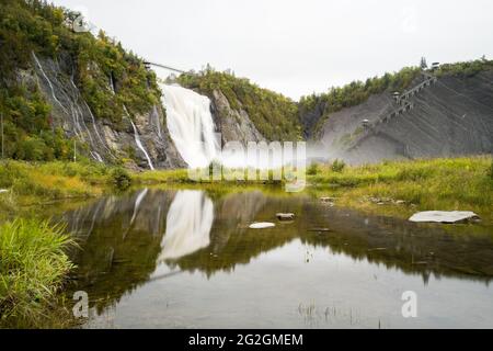 Blick auf die Montmorency Falls und die Brücke und ihre reflektierten Bilder im umliegenden Wasserbecken aus dem Erdgeschoss, Quebec, Kanada Stockfoto