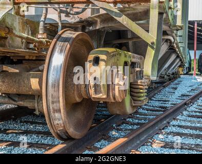 Nahaufnahme eines Eisenbahnrades auf einem Güterwagen mit Trichter verschlissen und rostig auf den Gleisen im Eisenbahnhof sitzend, bereit, einige Güter zu transportieren Stockfoto