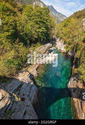 Schweiz, Tessin, Verzasca Valley, Verzasca, Taucher im Fluss am beliebten Becken mit den Granitfelsen. Der Doppelbogen der Ponte Romano (Ponti dei Salti) wirft Schatten in das smaragdgrüne Wasser. Stockfoto