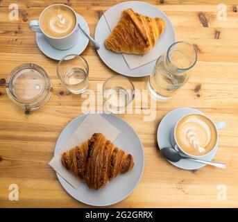 Tassen Latte-Kaffee und Croissants auf einem Holztisch Stockfoto