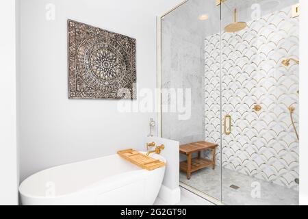 Eine wunderschöne geflieste Dusche und Badewanne mit Gold- und weißen Fliesen an den Wänden, Mosaikmarmorfliesen auf dem Boden und einem goldenen Duschkopf und Hardware. Stockfoto