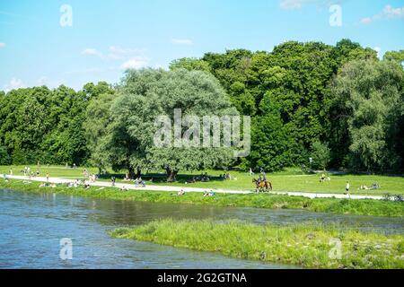 Nach den strengen Corona-Beschränkungen genießen die Menschen das Leben an einem warmen Sommertag am Ufer der Isar in München. Berittene Polizisten patrouillieren am Strand. Stockfoto