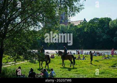 Nach den strengen Corona-Beschränkungen genießen die Menschen das Leben an einem warmen Sommertag am Ufer der Isar in München. Berittene Polizisten patrouillieren am Strand. Stockfoto