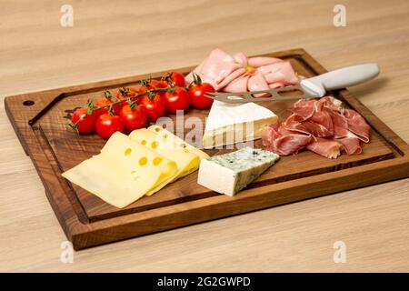 Nahaufnahme von verschiedenen Käsesorten, Fleisch und Kirschtomaten auf einem hölzernen Schneidebrett Stockfoto