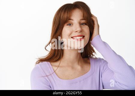 Schönheit und Wohlbefinden der Frauen. Lächelnd attraktives Mädchen berührt ihre Frisur, glücklich und entspannt, trägt niedliche Bluse, stehen gegen weiß Stockfoto