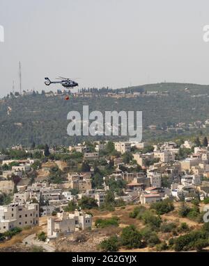 Abu Ghosh, Israel - 10. Juni 2021: Ein israelischer Polizeihubschrauber, ausgestattet mit einem Wasserbehälter, der zur Brandbekämpfung verwendet wird, auf dem Weg zu einem Feuer in der Nähe Stockfoto