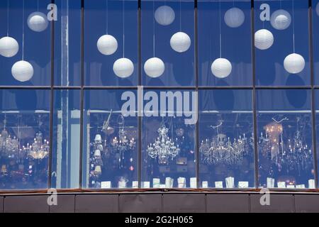 Kaufen Sie eine Leuchtenvitrine mit Kronleuchtern. Blick auf die Straße vom Fenster. Eine Auswahl an Kronleuchtern verschiedener Art im Laden. Stockfoto