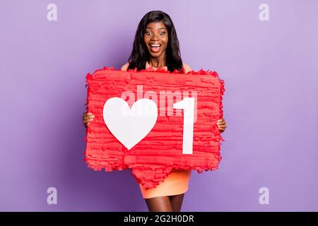 Foto von glücklich ziemlich dunkle Haut Mädchen tragen orange kurzen Rock halten große Papier wie Symbol isoliert auf violette Farbe Hintergrund Stockfoto