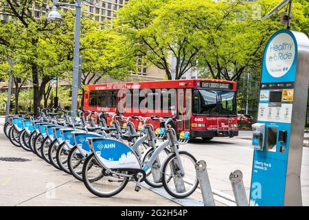 Pittsburgh, Pennsylvania, USA - 12. Mai 2021: Gesunde Fahrt mit dem Fahrrad Share Station mit roten öffentlichen Bus im Hintergrund. Es gibt 100 Stationen und Stockfoto