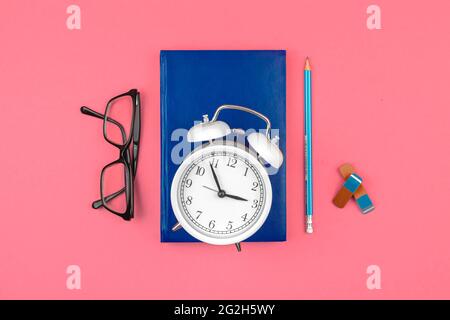 Schule rosa Arbeitsplatz mit Wecker, Notizbuch Tagebuch und Wecker auf dem Tisch Hintergrund, Draufsicht Stockfoto