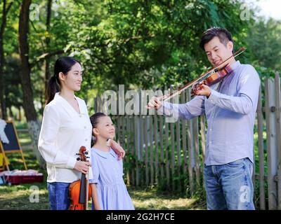Glückliche Familie von drei spielen Geige im Park hochwertige Foto Stockfoto