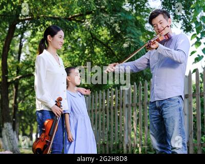 Glückliche Familie von drei spielen Geige im Park hochwertige Foto Stockfoto