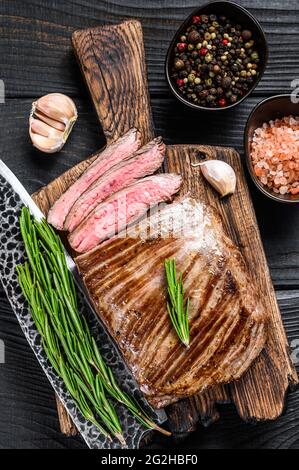 BBQ gegrillte Flanke oder Lasche Rindersteak auf einem hölzernen Schneidebrett. Schwarzer Holzhintergrund. Draufsicht Stockfoto