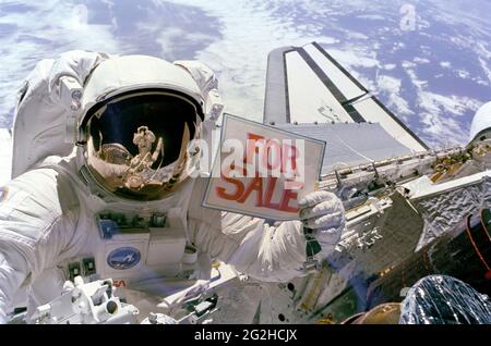 Astronaut Dale A. Gardner, der gerade den größten Teil seiner zweiten Extravehicular Activity (EVA)-Periode innerhalb von drei Tagen abgeschlossen hat, hält ein 'for Sale'-Zeichen hoch, das sich auf die beiden Satelliten Palapa B-2 und Westar 6 bezieht, die sie aus dem Orbit geholt haben, nachdem ihre Payload Assist Modules (PAM) nicht ausgelöst wurden. Astronaut Joseph P. Allen IV, der auch an den beiden EVAs teilgenommen hat, spiegelt sich in Gardners Helmvisier wider. Ein Teil von jedem der zwei wiederhergestellten Satelliten befindet sich in der unteren rechten Ecke, wobei Westar 6 näher an Discovery's Hinterteil liegt. Stockfoto