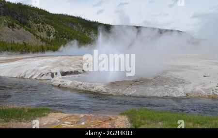 Spätfrühling in Yellowstone: Iron Spring Creek und ein ausbrechender Cliff Geyser der Emerald Group im Black Sand Basin Gebiet des Upper Geyser Basin Stockfoto