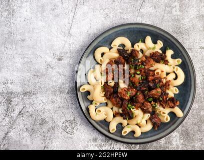 Schweinefleisch mit Pflaumen und Pasta auf einem runden Teller auf dunklem Grund geschmort. Draufsicht, flach liegend Stockfoto