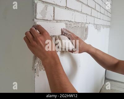 Verlegen von Gipskacheln in Reihen an der Wand mit männlichen Händen. Hausreparatur. Stockfoto