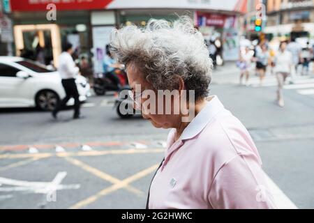 Taipei, Taiwan - 2. Juli 2018: Alte Frau, die im geschäftigen Geschäftsverkehr auf der Straße unterwegs ist Stockfoto