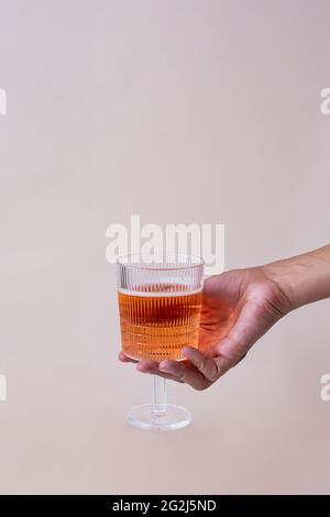 Weibliche Hand und Glas mit rosa Getränk auf pastellfarbenem Hintergrund. Kreatives Konzept des sommerlichen Cocktailgetränks. Stockfoto