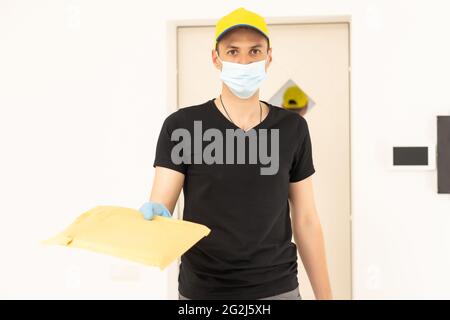 Der Versender trägt eine Maske und Handschuhe und beliefert den Online-Käufer mit Lebensmitteln nach Hause. Zu Hause bleiben Reduzieren Sie die Ausbreitung des Covid-19-Virus. Der Absender Stockfoto