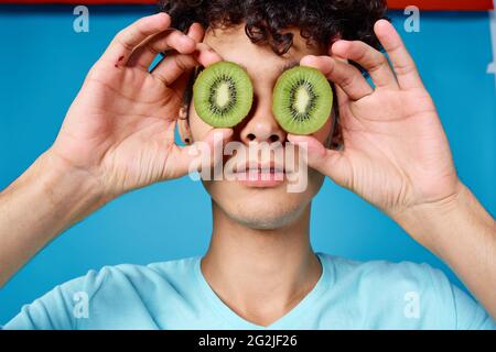 Mann mit lockigem Haar, der Kiwi in der Nähe des Klassengesichts hält Stockfoto