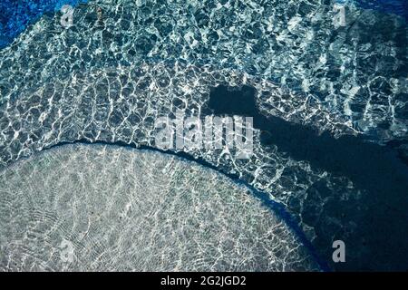 Sommerstimmung, plätschernde Wellen im Pool, Wabenmuster, Schatten zeigt Arm mit Kamera Stockfoto