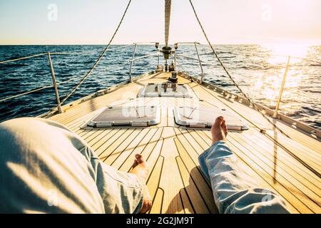 Pov Sicht der Mann Beine liegen und entspannen auf dem hölzernen Segelschiff Deck allein mit Sonnenuntergang im Hintergrund - Konzept der Reise Menschen und Freiheit im Sommerurlaub Stockfoto