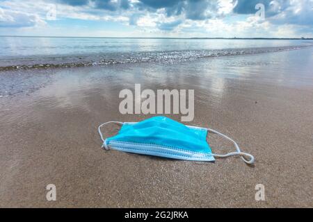 Schleswig-Holstein, Ostseeküste. Lübecker Bucht. Mund- und Nasenschutz, blaue Maske liegt am Strand. Stockfoto