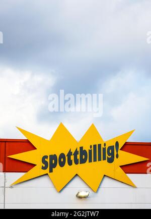 Mülheim, Nordrhein-Westfalen, Deutschland - schmutzbillig, Schriftzug auf der Fassade eines Spezialartikelmarktes vor bewölktem Himmel. Stockfoto