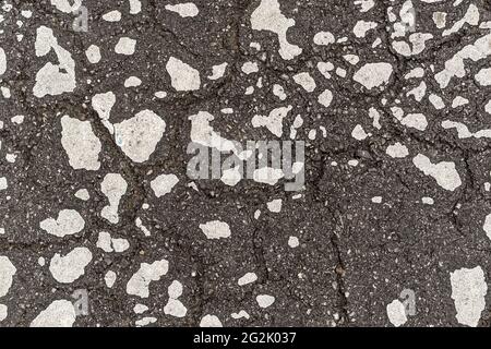 Eine alte dunkle Asphaltstraße mit Rissen und Flecken von alter, abblätternder weißer Farbe. Abstrakter Hintergrund Stockfoto
